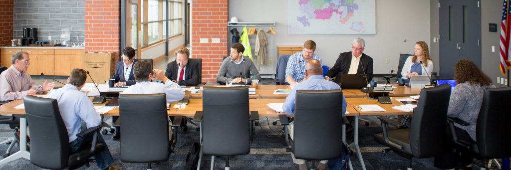 The Commissioners meet at a large table in-person.