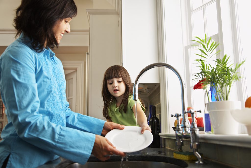 Adult female and young girl washing dishes at a kitchen sink to conserve water.
