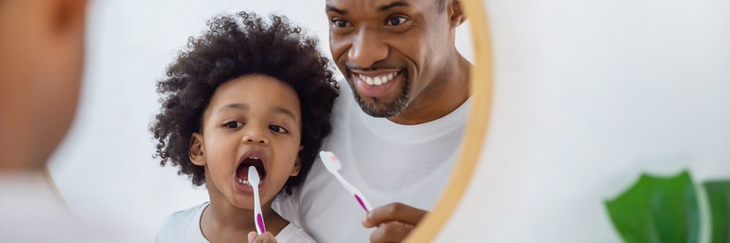 Father and child brushing teeth with resources at dental clinic.