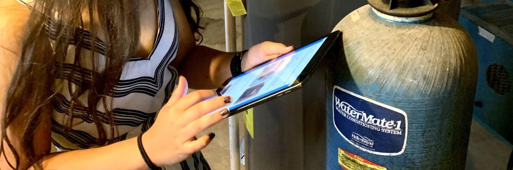 Woman uses the Salt Savers app on tablet at an old water softener or water conditioning system.
