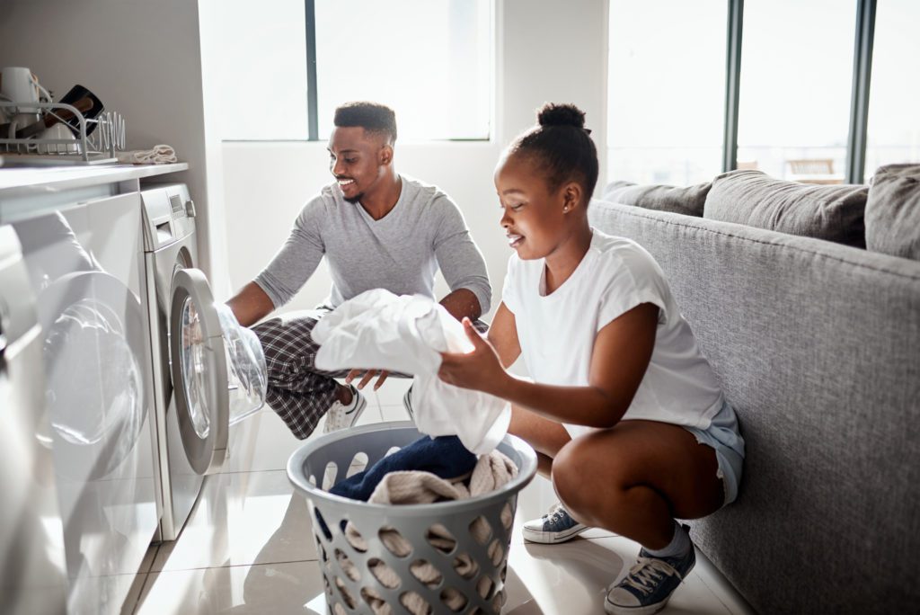 Multicultural couple in front of washer and dryer doing laundry in their home.
