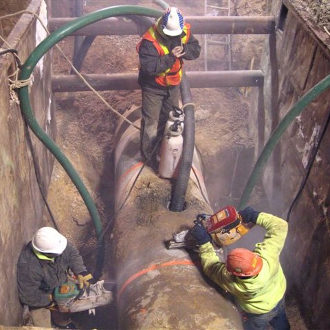 Three workers in hardhats cut a damaged section of forcemain pipe for removal.