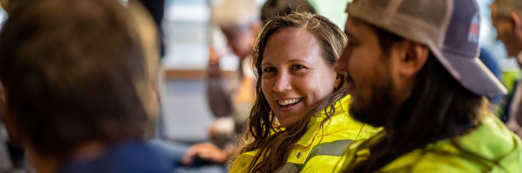 Wastewater operators talk at a staff meeting; a female operator talks to two blurred male operators.