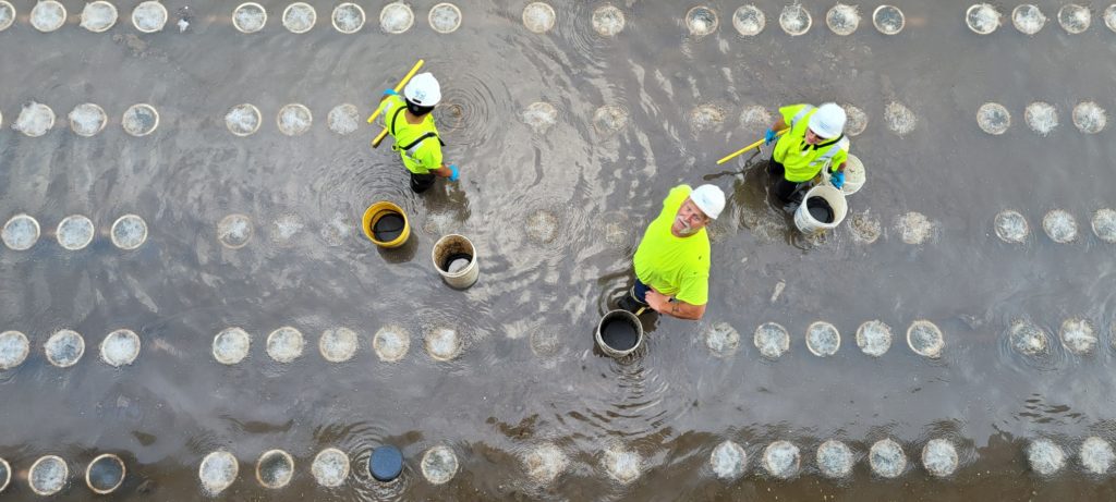 Three staff members clean a drained aeration tank, wearing waders and hard hats.