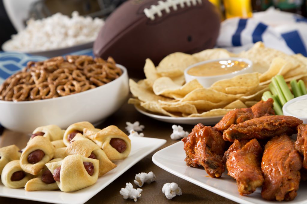 Hot wings, nachos, pigs in a blanket, pretzels, beer and popcorn for a football or tailgate party spread.
