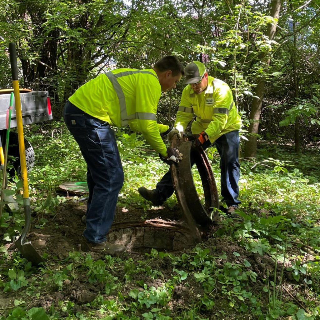 Two men remove the cast-iron manhole frame.