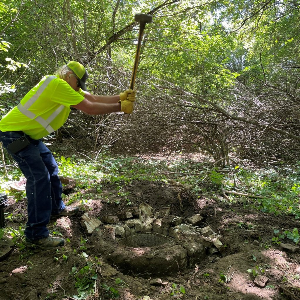 A man uses a sledgehammer to break up a deteriorated manhole ring.