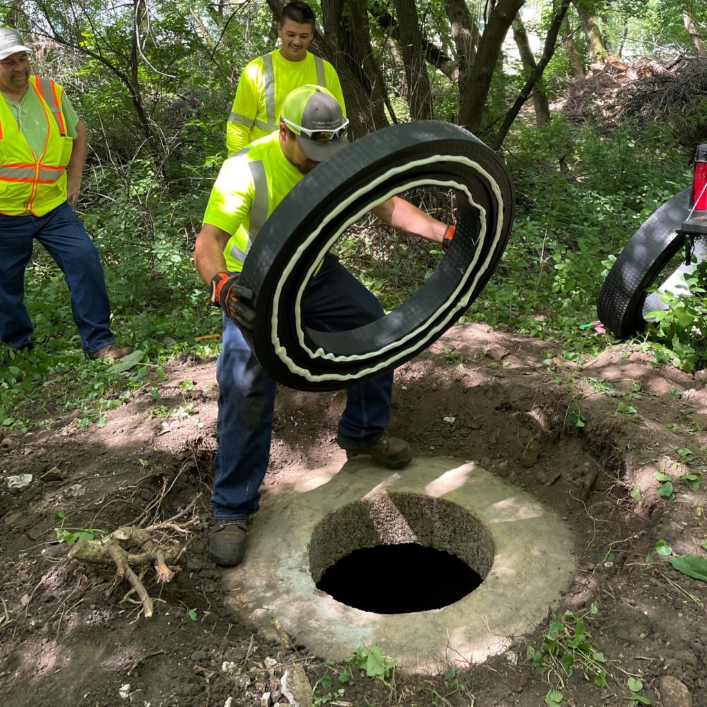 A man places a plastic ring with adhesive applied on the top deck of the manhole.