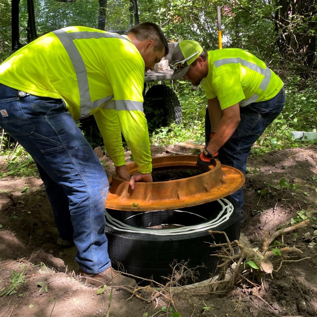 Two men place the manhole cover frame back on top of newly installed plastic rings.