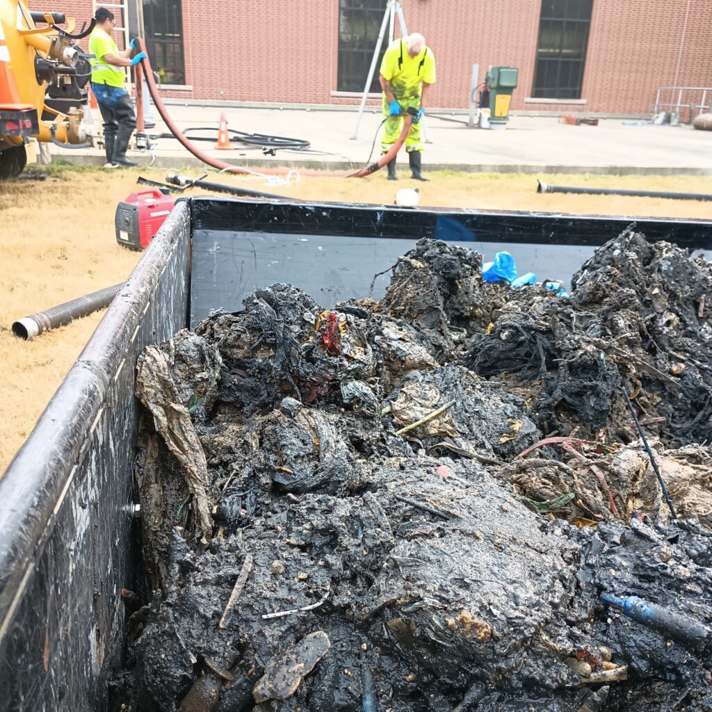 A close up of removed rags from the WAS blend tank, with workers Rigo Ramon-Solis and Bart Nelson picking up hoses in the background.