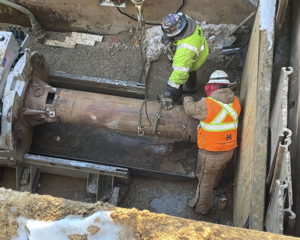 Contractors add 16-inch auger casing pipe to the reamer head. The reamer head is connected to the last pilot tube.
