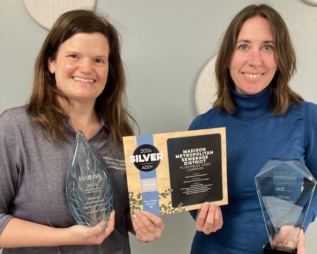 Communications team members Amanda Wegner and Amy Steger hold some of the awards received for the Flushables video campaign.
