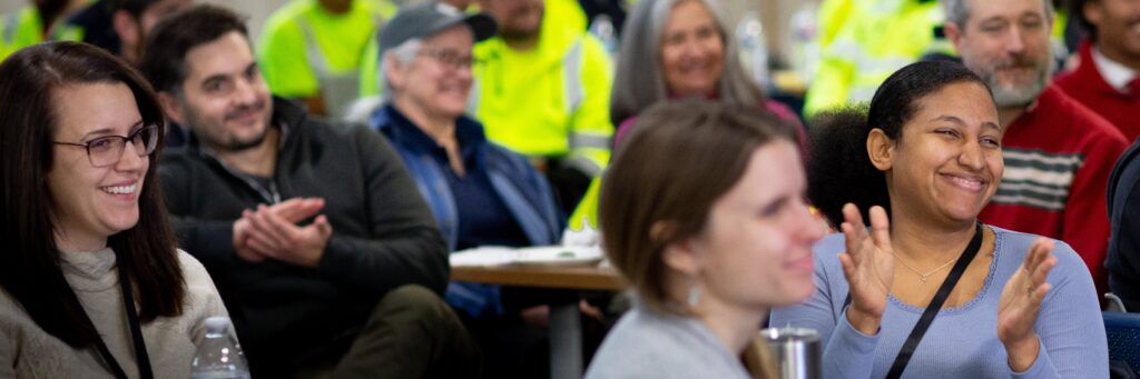 A crowd of District staff claps in the audience at a meeting.