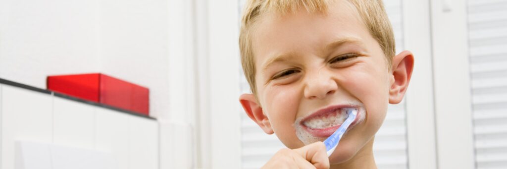 A small child brushes his teeth. Toothpaste foams around his mouth.