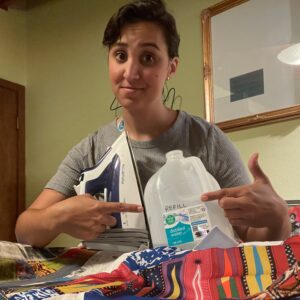 A woman at an ironing board with an iron and refillable bottled water.