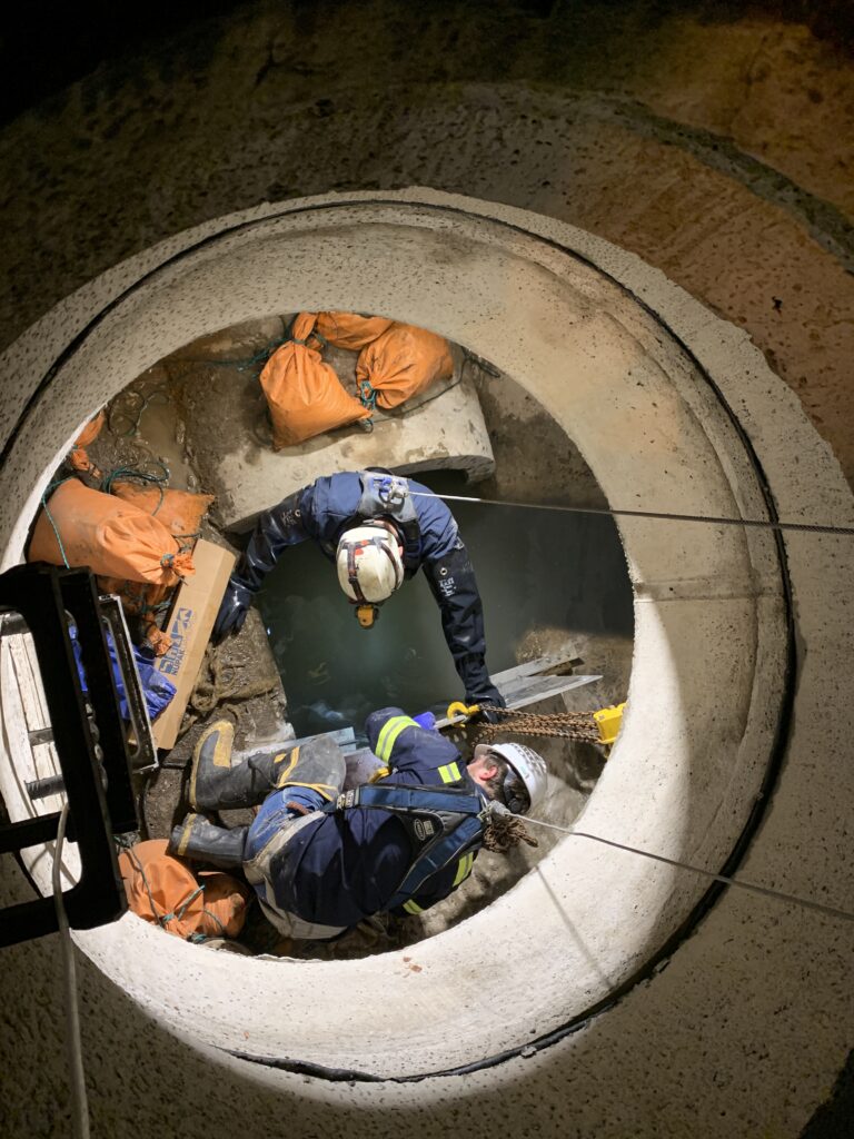 Locator Kody Wright and mechanic Corey Stark-Prohaska install the stop plate to divert the flow from the damaged pipe.