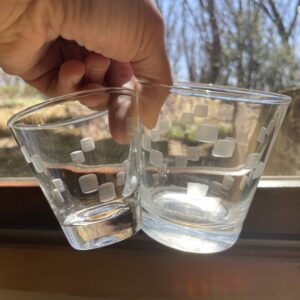 A hand holding two glasses, clear on the left and etched glass on the right.