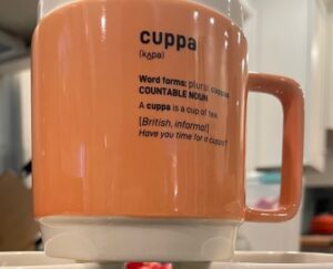 An orange mug with the word "cuppa" and its definition printed on the side.