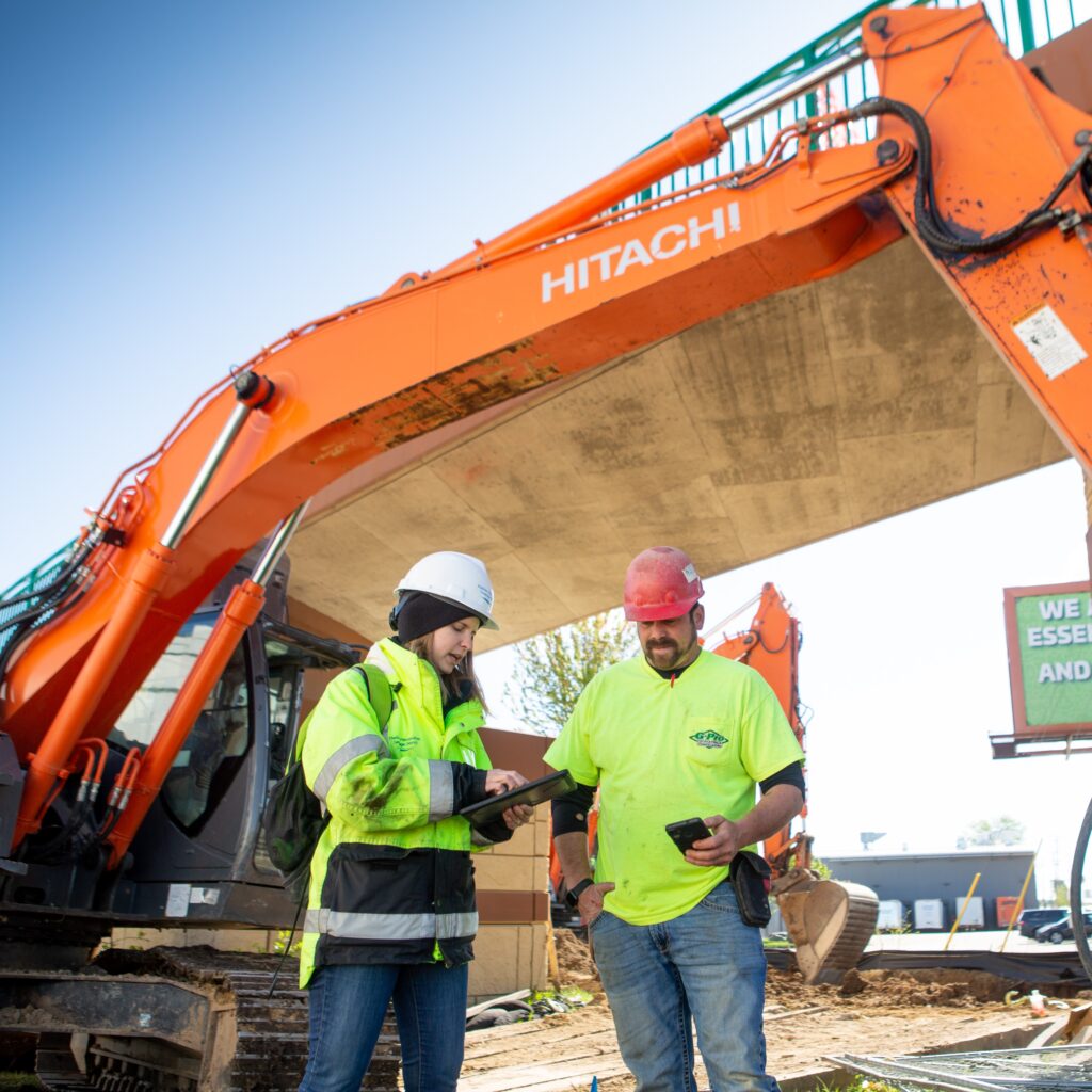 An engineer talks with a contractor on the construction site with large equipment behind them.