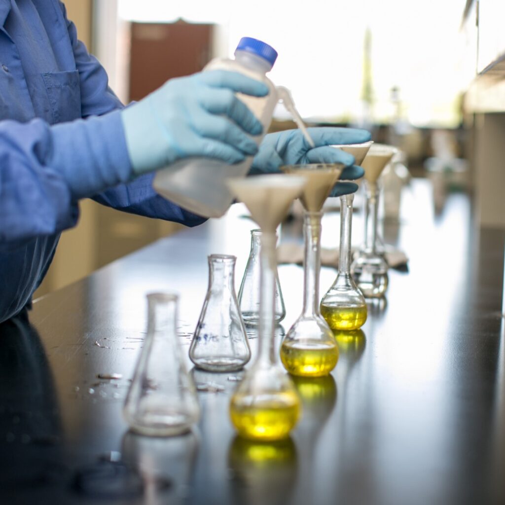 A chemist adds sample material to a row of flasks and beakers in the lab.
