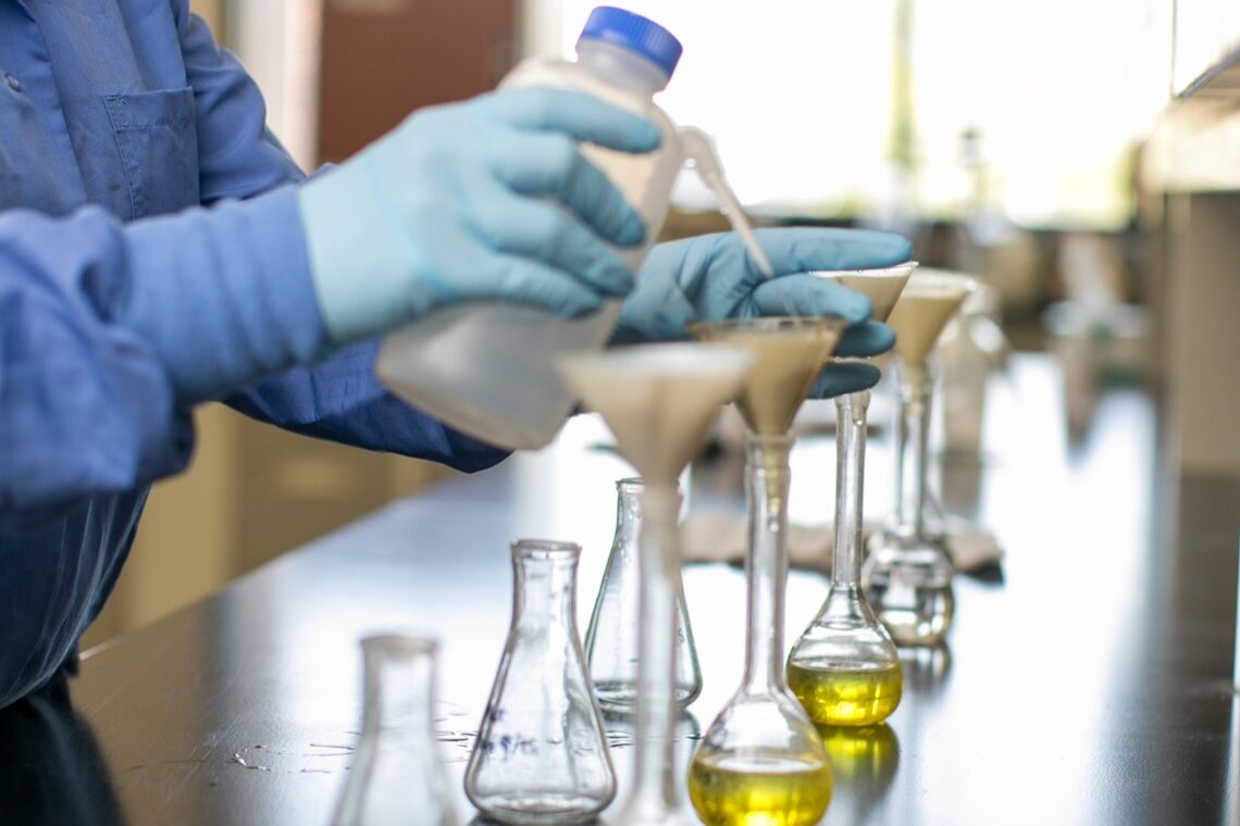 A chemist adds sample material to a row of flasks and beakers in the lab.