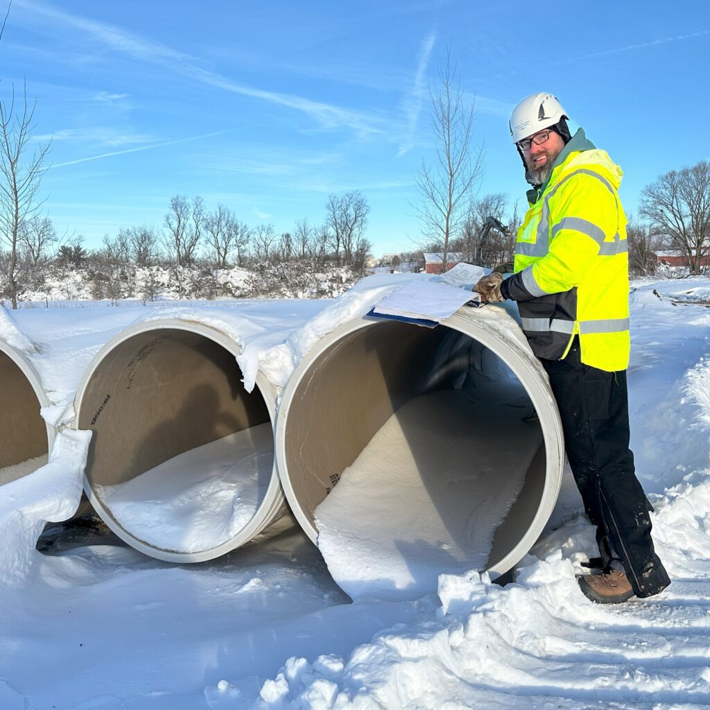 An engineer reviews paperwork on sewer pipes at a snow-covered construction job site in winter.