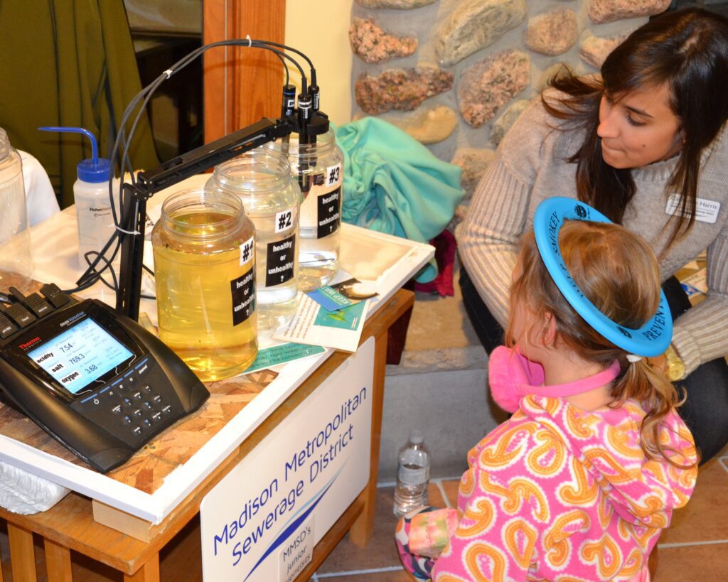 A young explorer examines a water science exhibit while District staff assist.