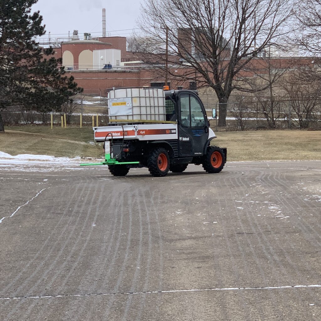 A bobcat with a tank applies brine at the treatment plant.