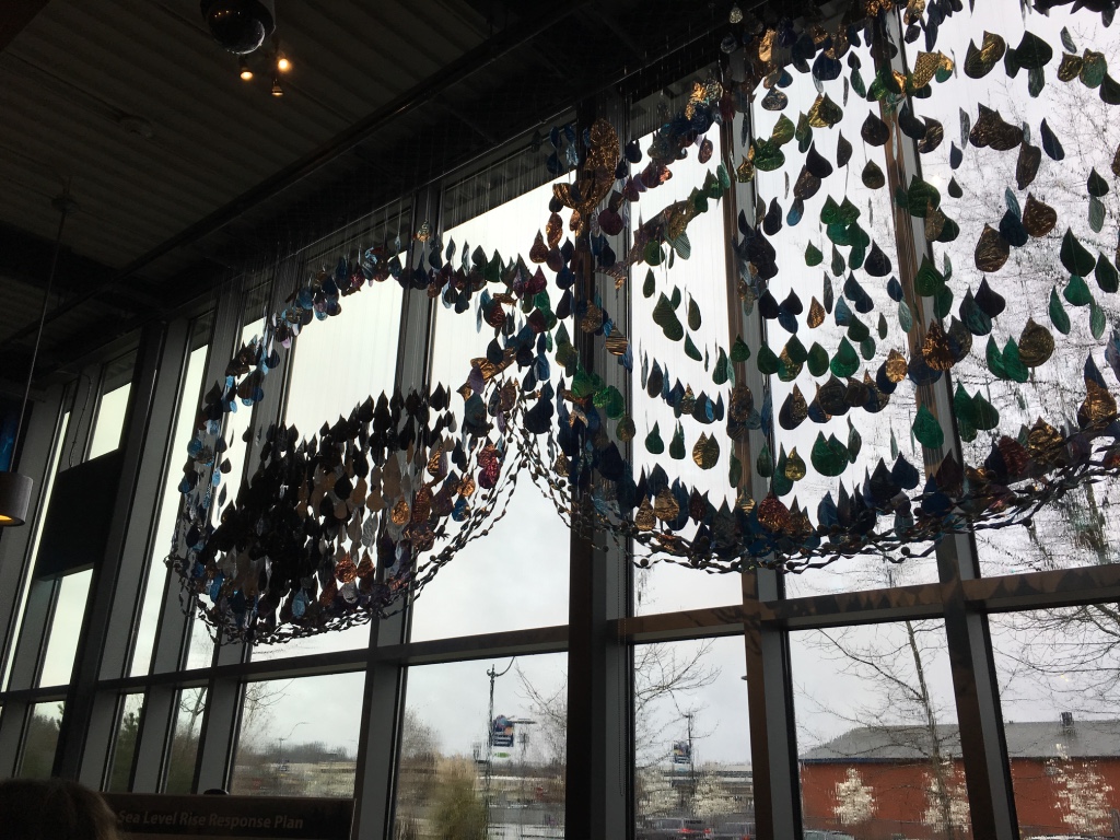 An artistic water droplet installation hanging from the ceiling in front of a window.