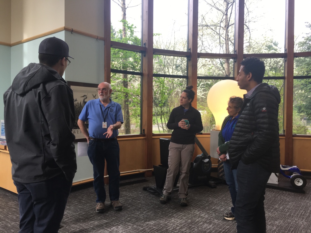 A small group of people talks in a water education area of a building.
