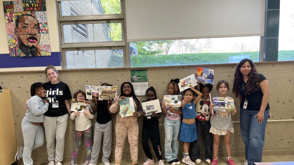 A group of nine smiling students showing the water-themed collages they created alongside a teacher and a Pollution Prevention staff member.