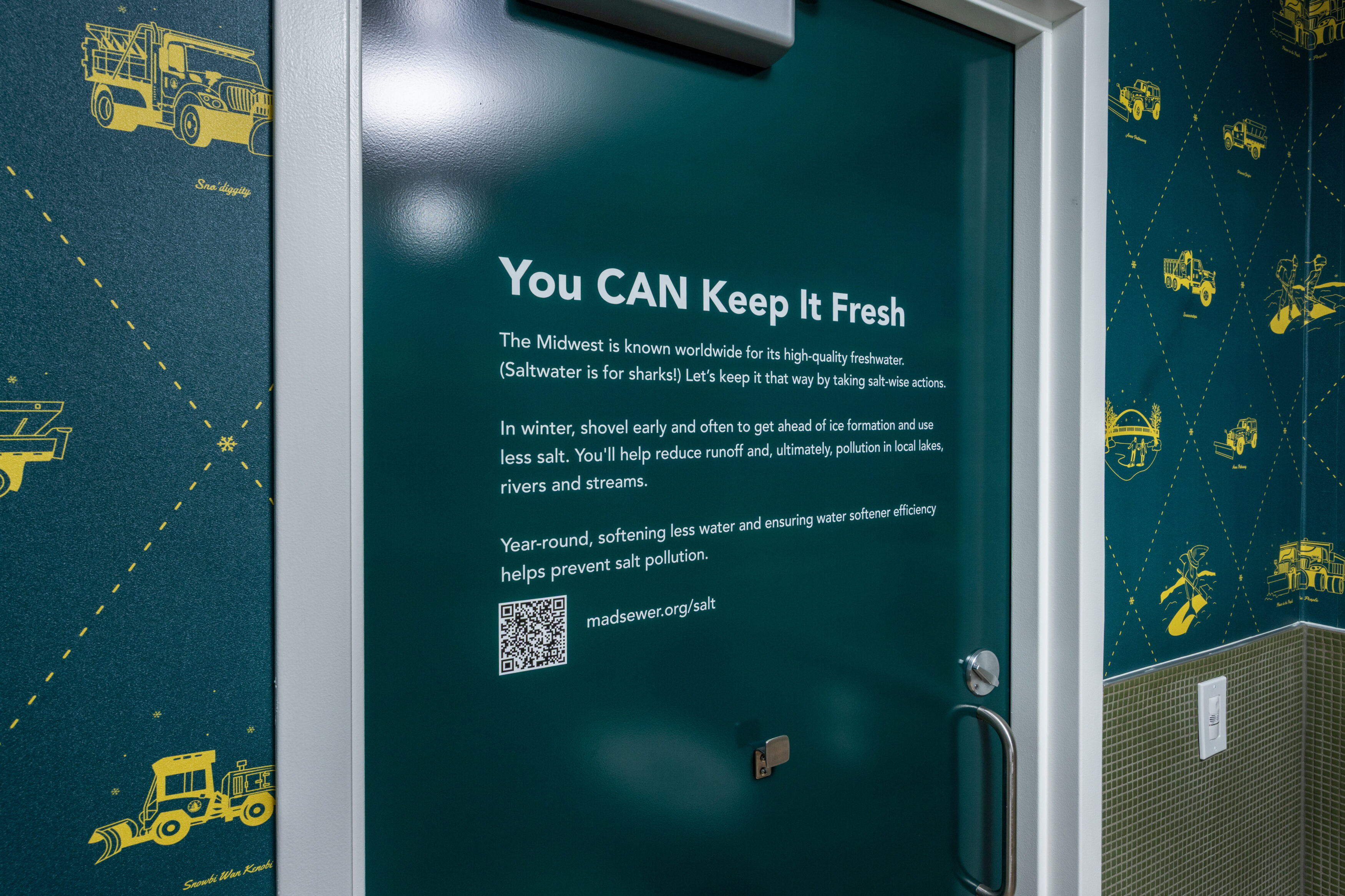 The chloride-themed bathroom at Madison Public Market features snow removal vehicles on the wallpaper and shares salt-reduction messaging on the door. The chloride-themed bathroom at Madison Public Market features snow removal vehicles on the wallpaper and shares salt-reduction messaging on the door.